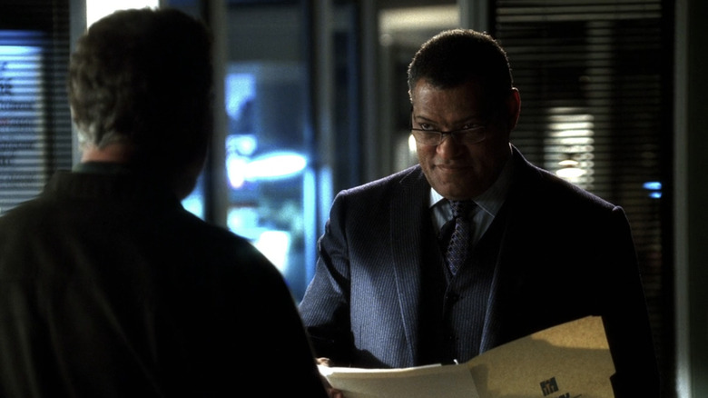 Laurence Fishburne as Raymond Langston smiles as he holds a file and stands opposite someone with their back to the camera in CSI