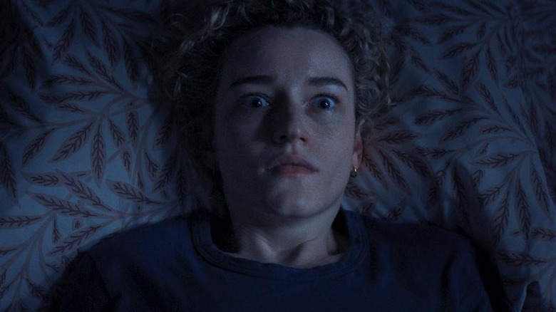 Julia Garner as Justine laying in bed with a shocked look on her face in Weapons